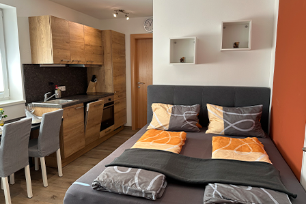 Appartement Rupert – Doppelbett und gemütliche Farbakzente Thumbnail Gemütliches Doppelbett mit warmen Orangetönen im Appartement Rupert am Gut Maierleben.